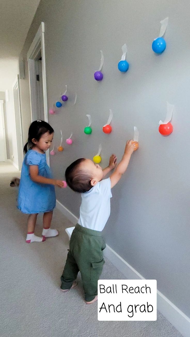 two young children are playing with colorful balls on the wall in an empty room that says ball reach and grab