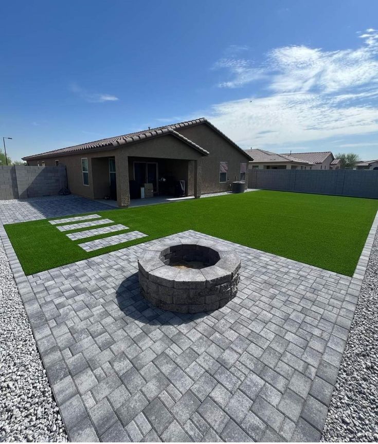 a brick patio with a fire pit in the middle and grass on the other side