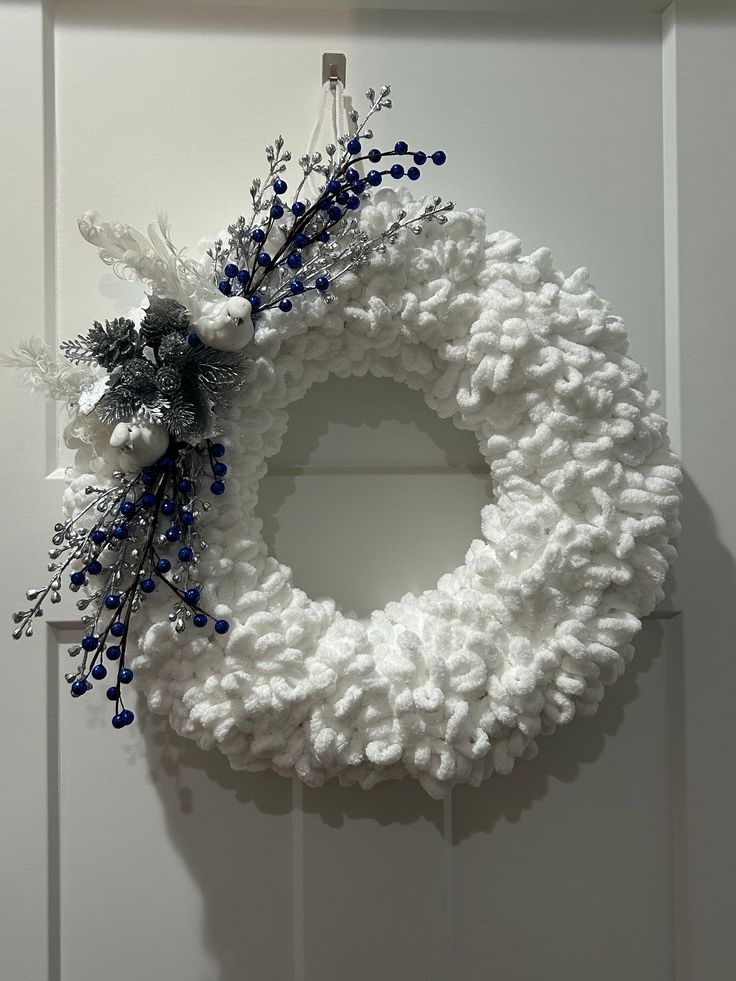 a white wreath with blue berries hanging on a door