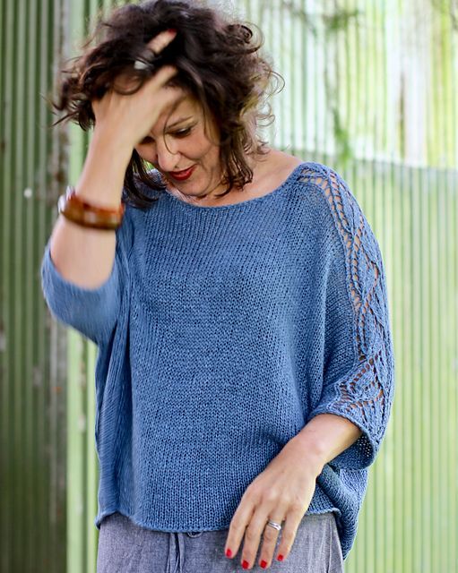 a woman standing in front of a green wall with her hands on her head and wearing a blue sweater