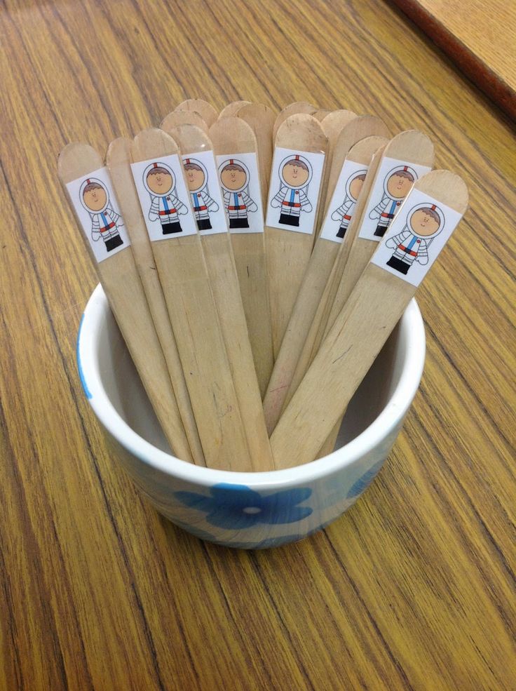 six wooden spoons in a bowl with cartoon stickers on the handles, sitting on a table