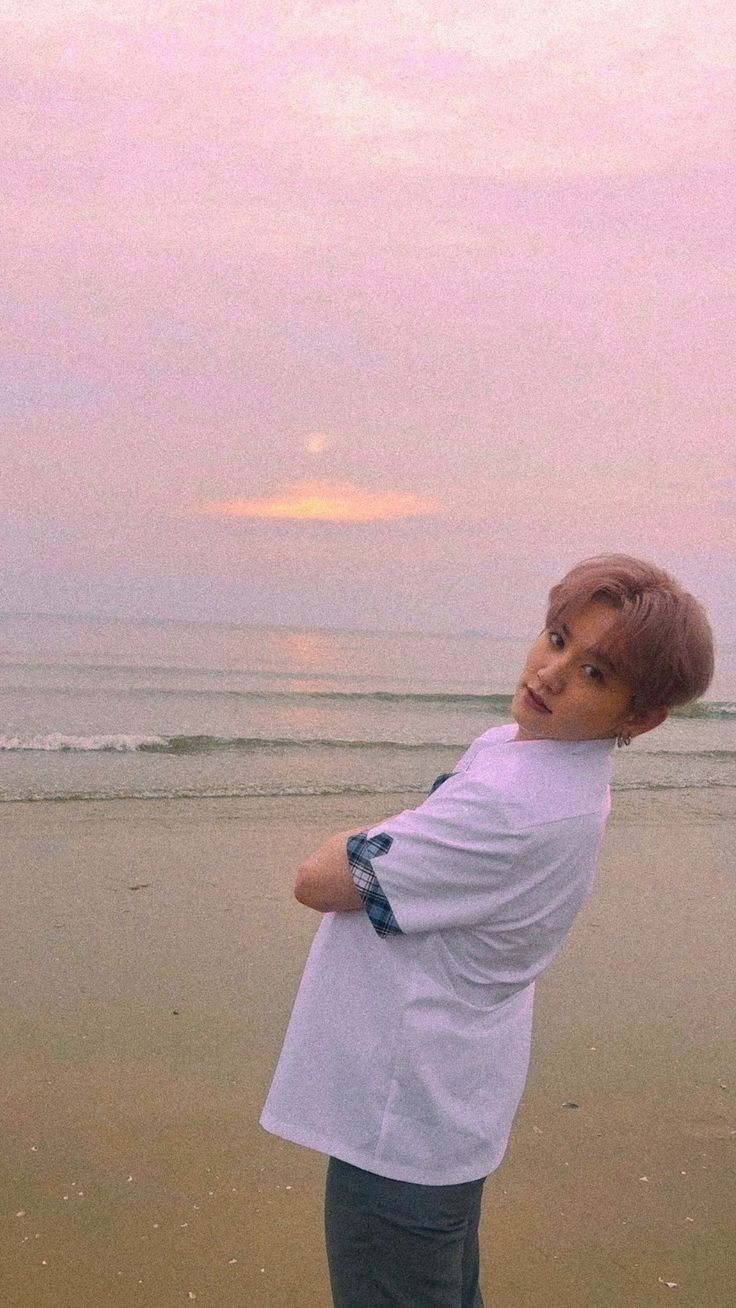 a young boy standing on top of a sandy beach next to the ocean at sunset