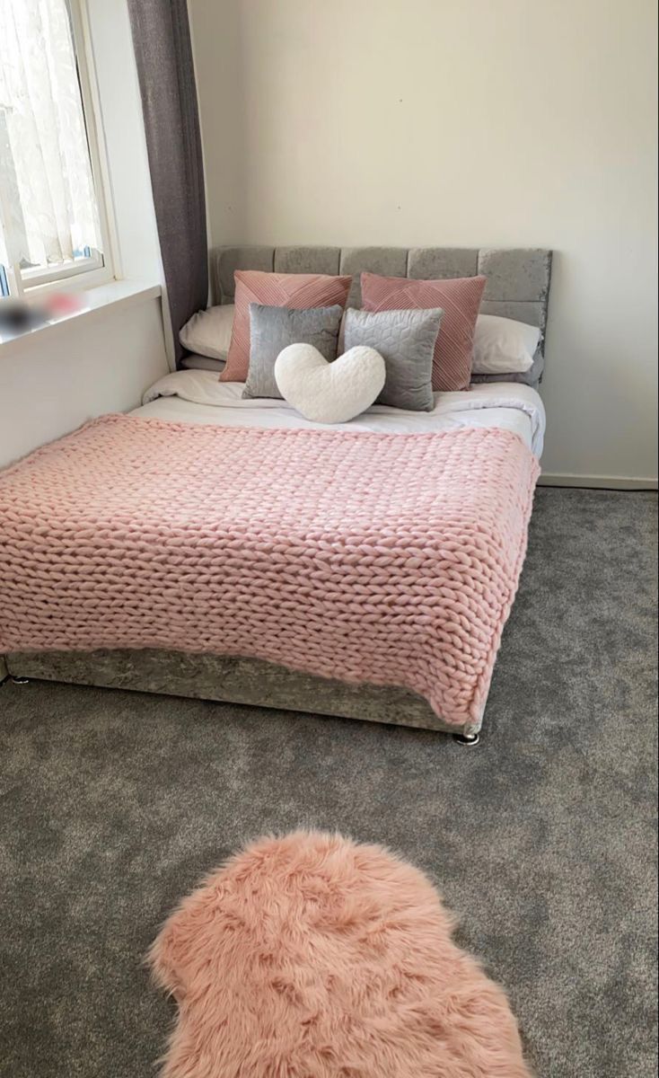 a bed with pink blankets and pillows in a small room next to a window on the floor