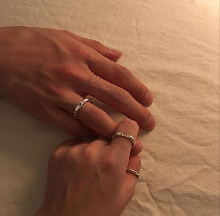 two hands holding each other on top of a bed with white sheets and pillows in the background