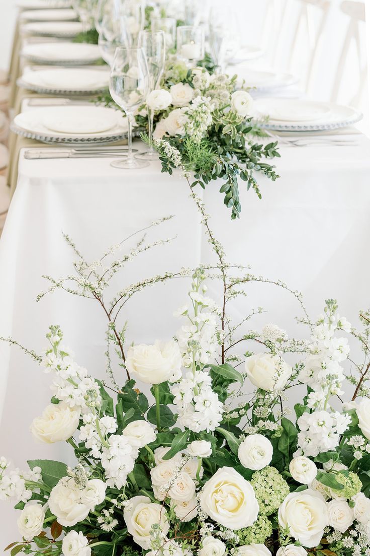 the table is set with white flowers and greenery