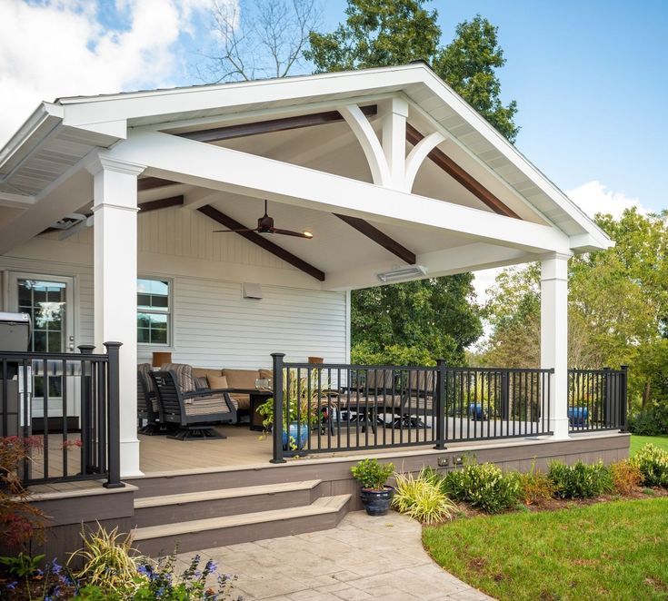 a covered patio with black railings and white walls, surrounded by green grass and trees