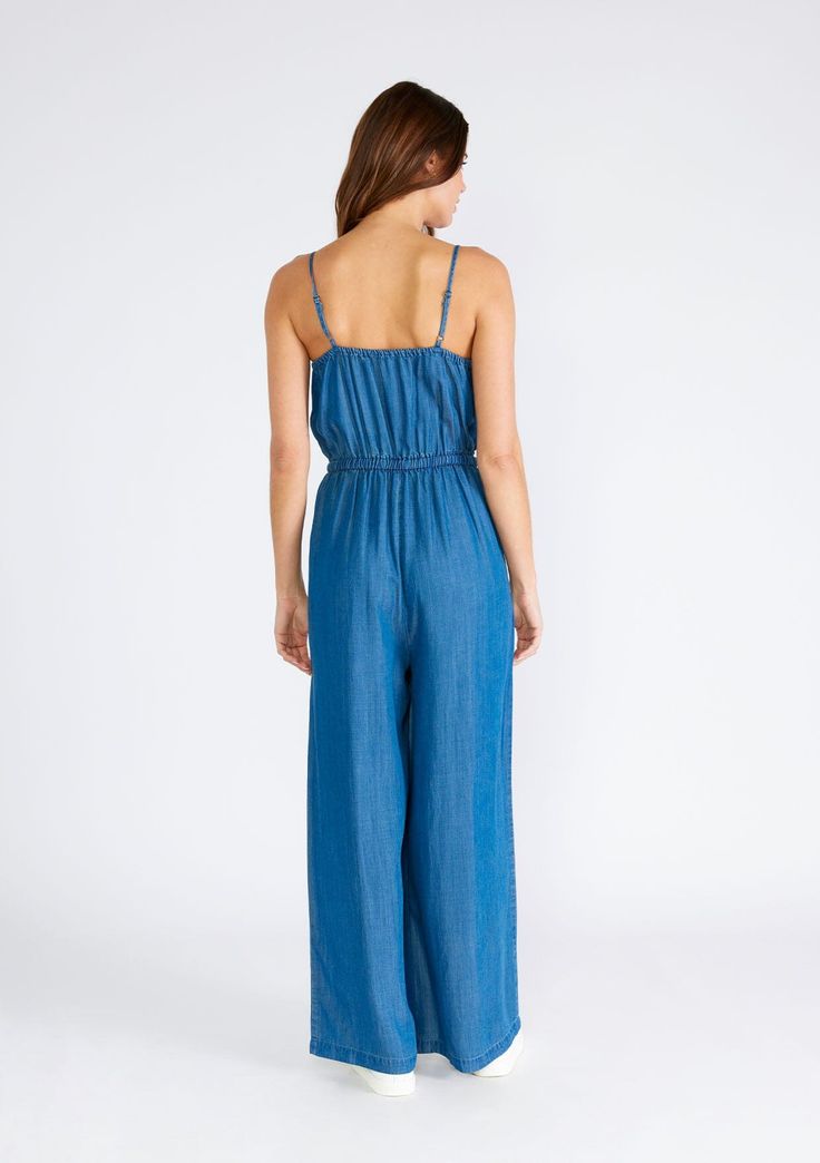 A classic wide-leg sleeveless jumpsuit crafted from denim blue tencel. Tencel Relaxed fit Sleeveless Long wide leg Scoop neckline Adjustable spaghetti straps Adjustable drawstring tie waist Self-covered button front top Elastic waist Side pockets Bohemian jumpsuit A bold denim blue wash adds a fresh touch to this timeless sleeveless jumpsuit. An effortless one-and-done style with a trendy long wide leg, a flattering scooped neckline, and adjustable spaghetti straps. Crafted from lightweight tenc Casual Strapless Sleeveless Jumpsuit With Elastic Waistband, Casual Strapless Jumpsuit With Elastic Waistband, Summer Strapless Jumpsuit In Medium Wash, Casual Medium Wash Strapless Jumpsuit, Summer Strapless Medium Wash Jumpsuit, Casual Strapless Jumpsuit In Medium Wash For Spring, Casual Strapless Jumpsuit For Spring In Medium Wash, Casual Medium Wash Strapless Jumpsuit For Spring, Casual Sleeveless Overalls With Tie Straps