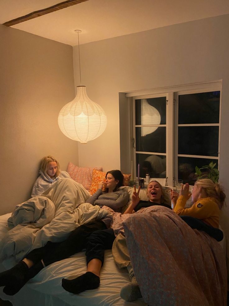 three people laying on a bed in a room with two lamps hanging from the ceiling