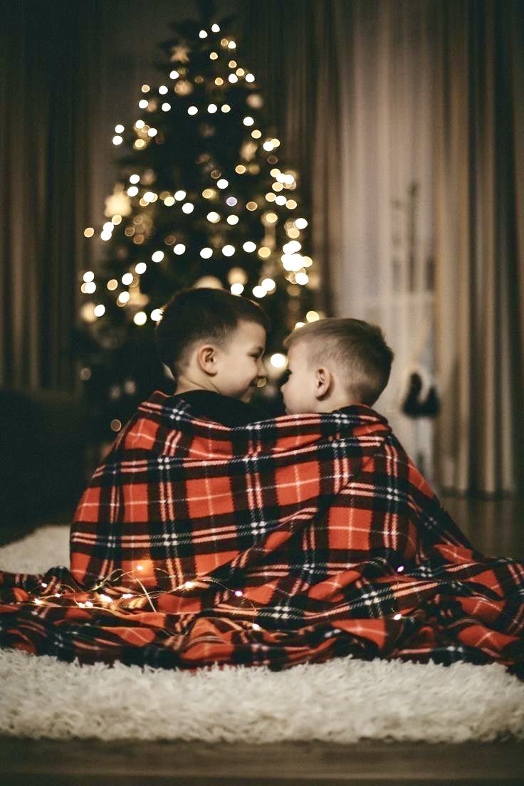 two young boys wrapped up in blankets sitting next to a christmas tree