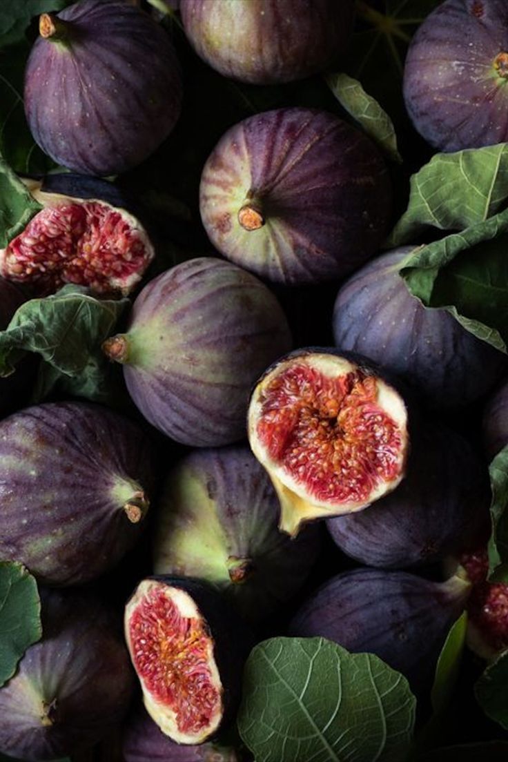 figs with green leaves and one cut in half on the top, sitting next to each other