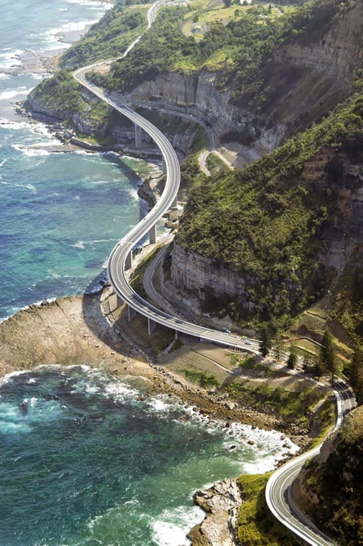 an aerial view of a highway near the ocean with waves crashing on it's sides