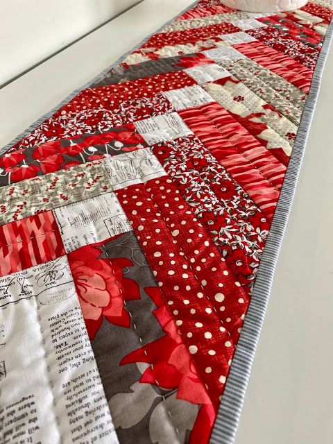 a red and white quilted table runner on a window sill with flowers in the center