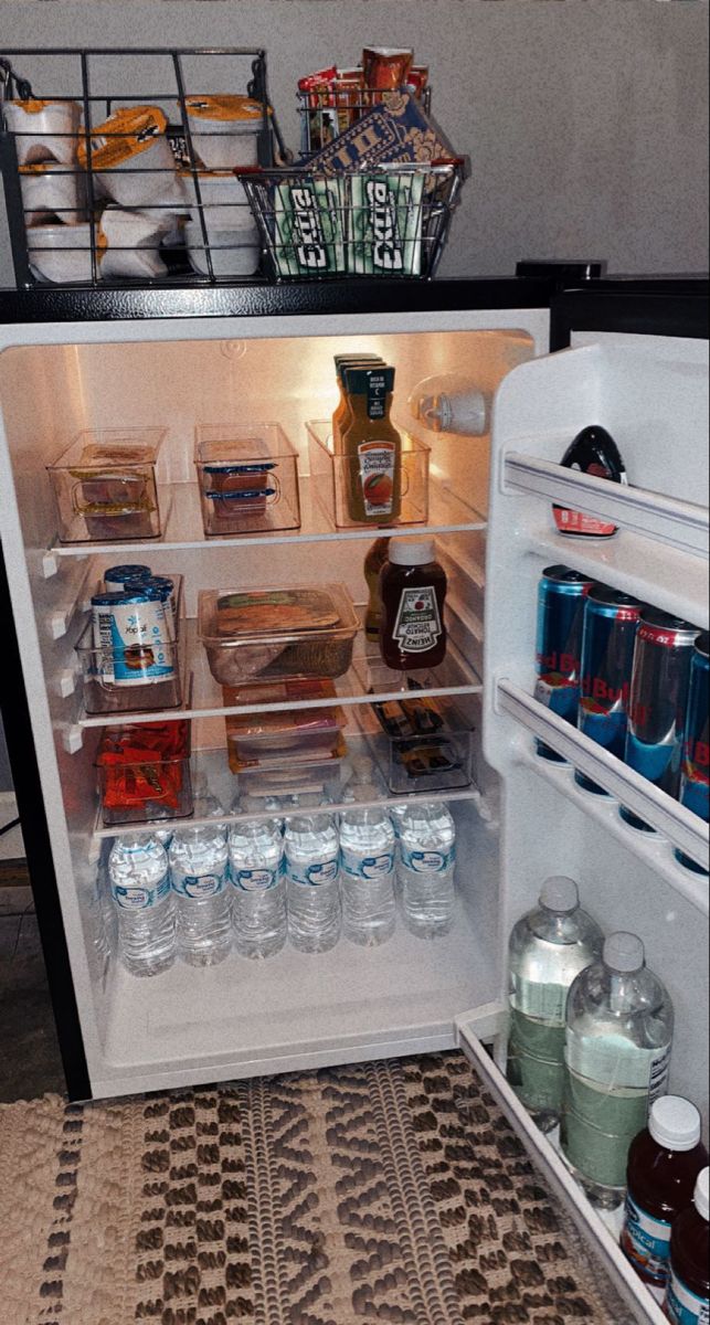 an open refrigerator filled with lots of food and drinks on top of a tiled floor