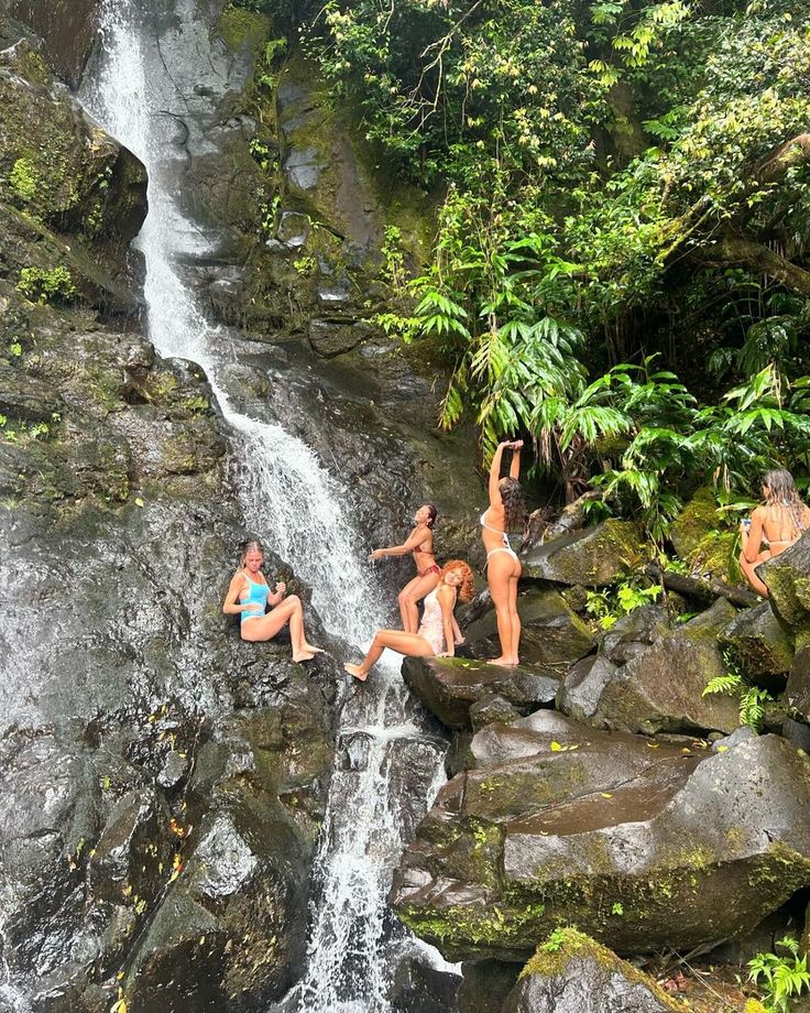 four people are sitting on rocks in front of a waterfall and posing for the camera