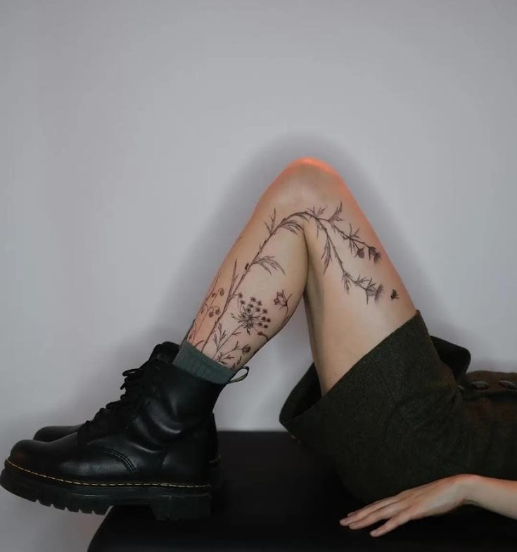 a woman's legs with tattoos sitting on top of a black bench next to a white wall