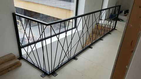 a balcony railing with black iron bars on the top and bottom, in front of a window