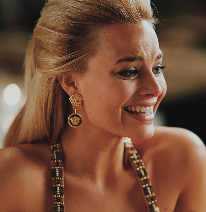 a woman wearing gold jewelry and smiling at the camera with her hand on her hip