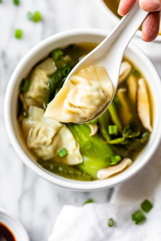 someone holding a spoon full of dumplings and broccoli in a white bowl