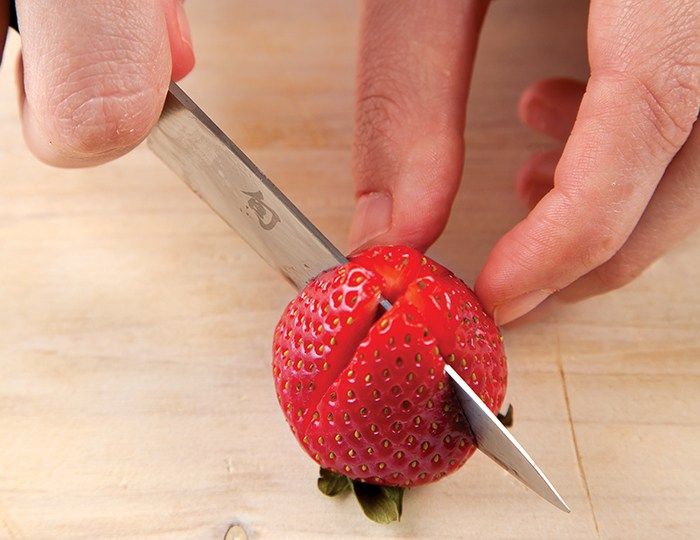 a person cutting up a strawberry with a knife