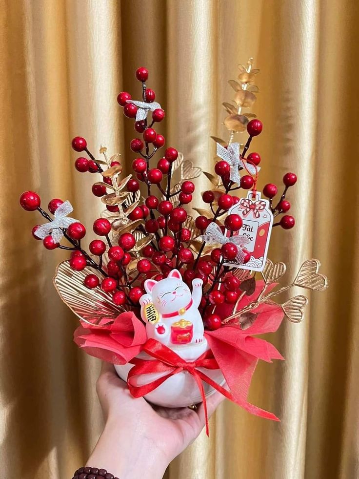 a person is holding a bouquet with red berries and other decorations on it in front of a gold curtain