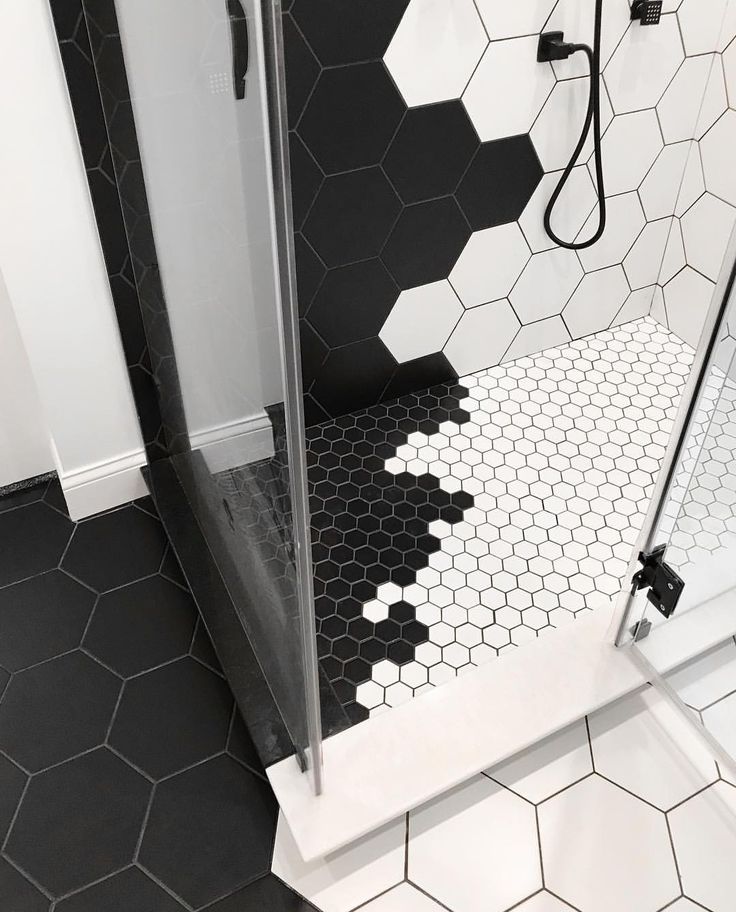 a black and white tiled bathroom with hexagonal tiles on the floor, shower stall and standup shower