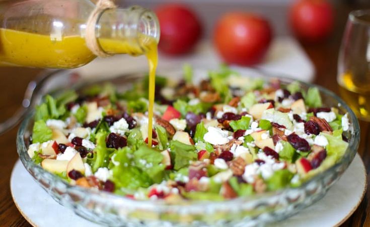 someone pouring dressing onto a salad in a bowl