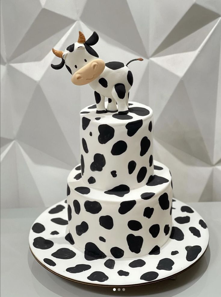 a three tiered cake decorated with black and white polka dots has a cow figurine on top