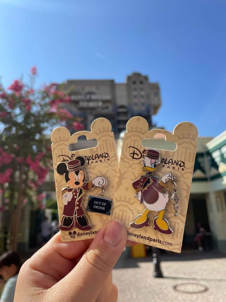 someone holding up two disney pins in front of a building