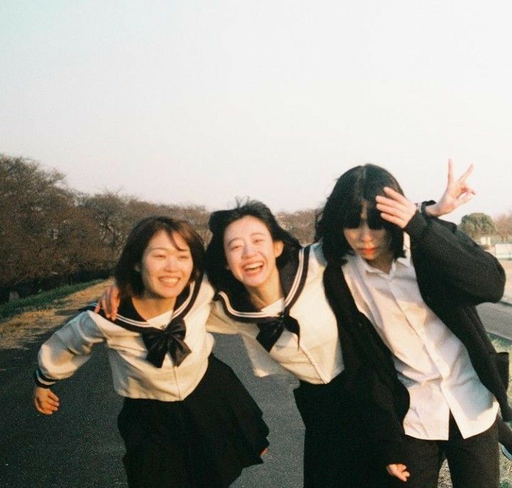 three young women posing for a photo on the side of a road with trees in the background