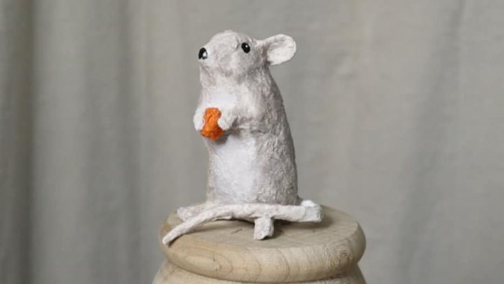 a toy mouse is sitting on top of a piece of wood and holding a carrot