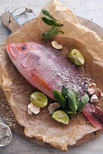 a fish is sitting on a plate with some herbs and seasoning next to it