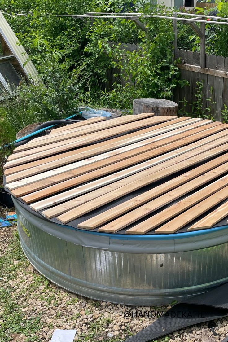 A wood-slatted cover is sitting on top of a metal stock tank pool. Stock Tank Pool Hot Tubs, Stock Tank Pool Cover, Stock Tank Pool Deck, Stock Pool, Stock Tank Pool Ideas, Galvanized Stock Tank, Stock Tank Swimming Pool, Cowboy Pool, Stock Pools