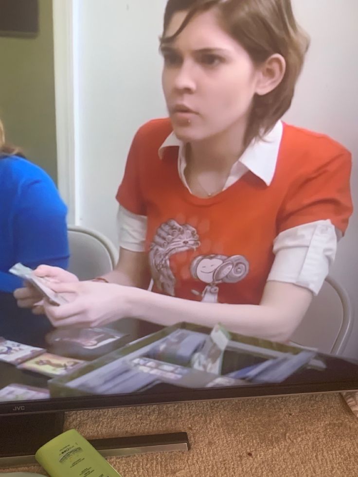 a woman sitting at a table in front of a tv screen holding a remote control