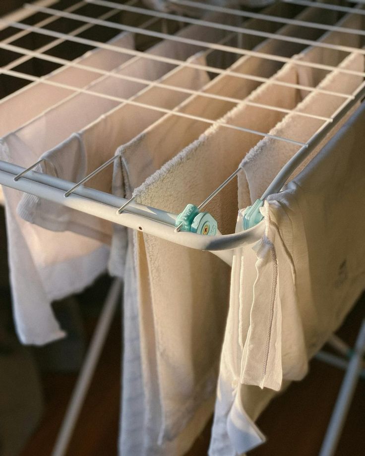 clothes are hanging on a drying rack in a room with wooden floors and white linens