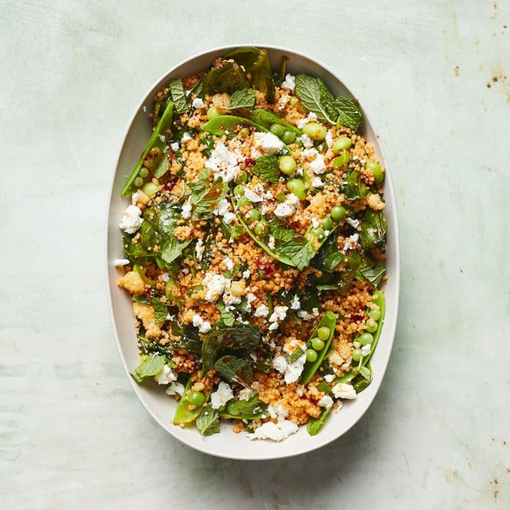 a white bowl filled with green vegetables and feta cheese