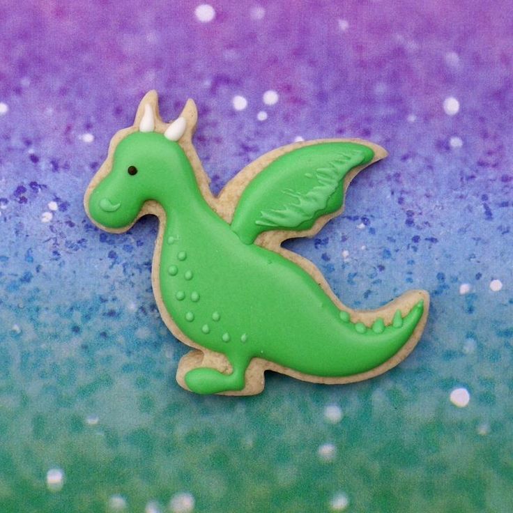 a green dragon cookie sitting on top of a blue and purple background