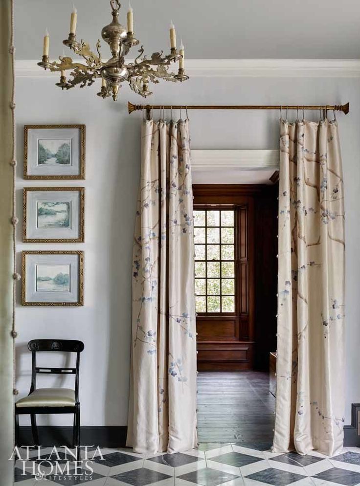 a chandelier hangs from the ceiling in front of two windows with drapes