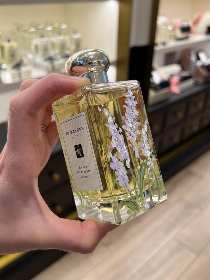 a hand holding a bottle of perfume in front of a store display case with flowers on it