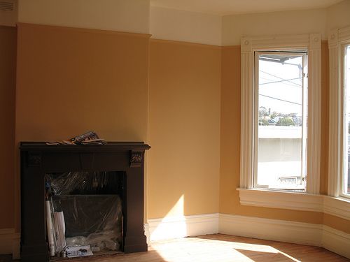 an empty room with two windows and a fire place in the corner that has been painted orange