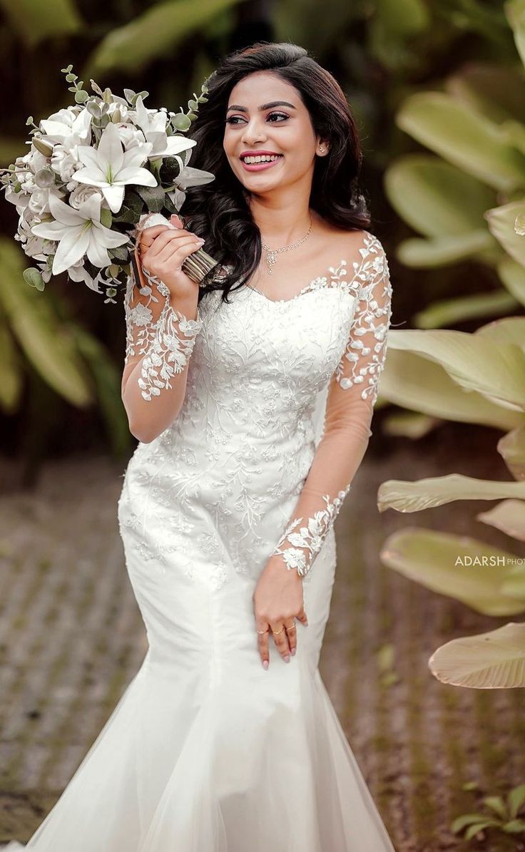 a woman wearing a wedding dress holding flowers in her hand and smiling at the camera