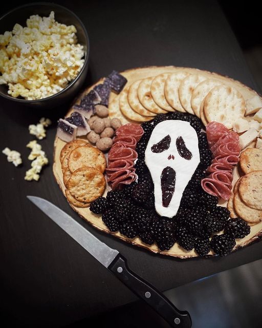 a platter with crackers, blackberries, cheese and meats in the shape of a ghost