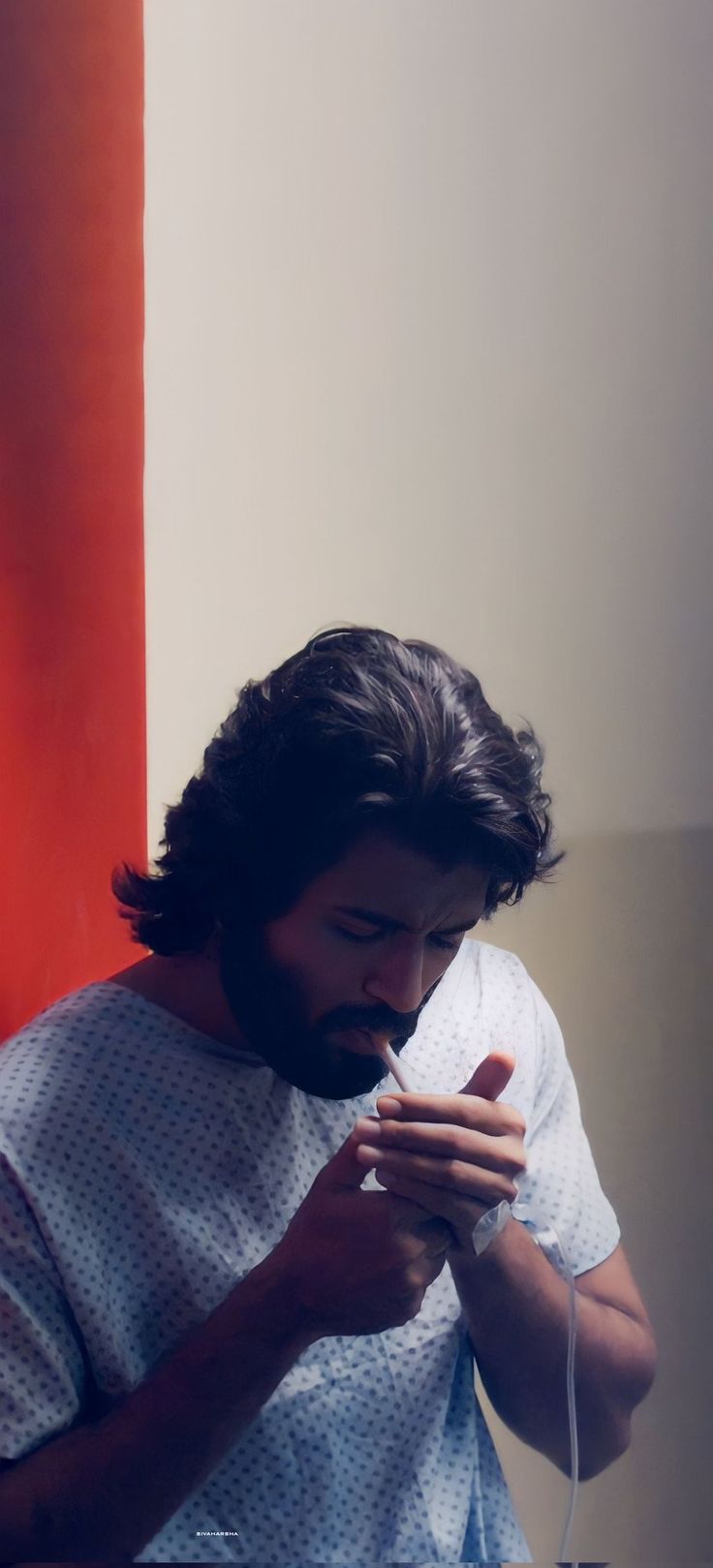 a man with long hair and beard is looking at his cell phone while standing in front of a red wall