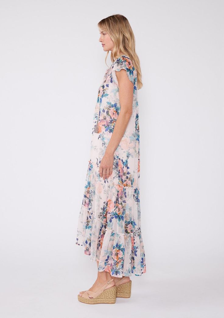 Our ultra-relaxed bohemian maxi dress is designed in a beautiful pink and blue floral print and features short flutter sleeves and flowy ruffle-trimmed high-low skirt. Dress it up with a a cute wedge for your next special occasion, or pair it with easy boho flat sandals for a relaxed spring/summer outfit. Floral print Chiffon Relaxed fit Short flutter sleeves High-low skirt Adjustable tie cuffs Maxi length Ruffle-trimmed tiered skirt Round neckline with tassel ties Button front Contrast bib Shee Bohemian Midi Dress With Ruffle Sleeves For Spring, Spring Floral Boho Print Flowy Dress, Spring Flowy Floral Dress With Boho Print, Summer Beach Midi Dress With Ruffle Sleeves, Spring Floral Dress With Boho Print, Spring Floral Dress With Boho Print And Flowy Fit, Flowy Floral Dress With Boho Print For Spring, Floral Print Flowy Short Sleeve Maxi Dress, Flowy Short Sleeve Maxi Dress In Breezy Style