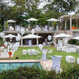 an outdoor wedding venue with white chairs and umbrellas set up in front of the pool