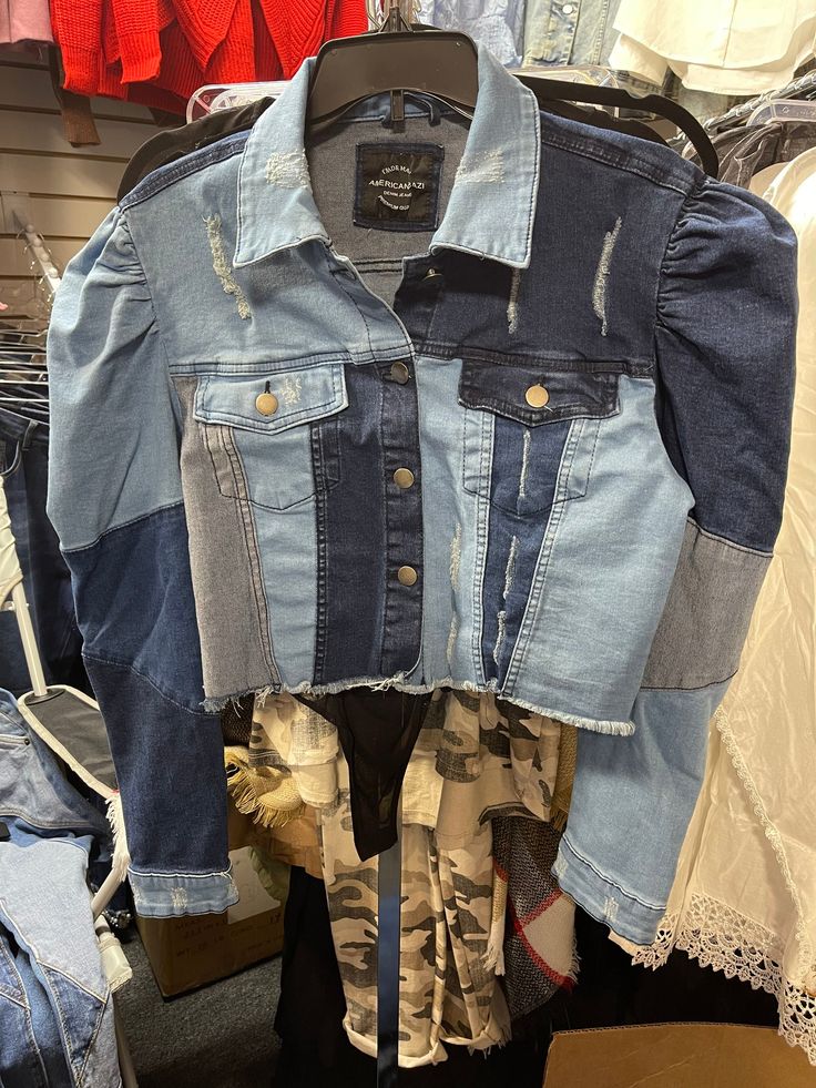 an old jean jacket is hanging on a rack in a clothing store with other clothes