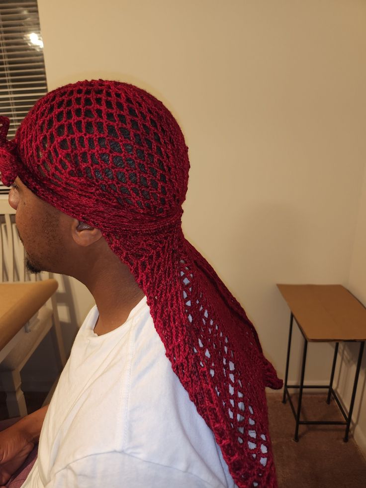 a man wearing a red knitted hat and scarf on top of his head in front of a table