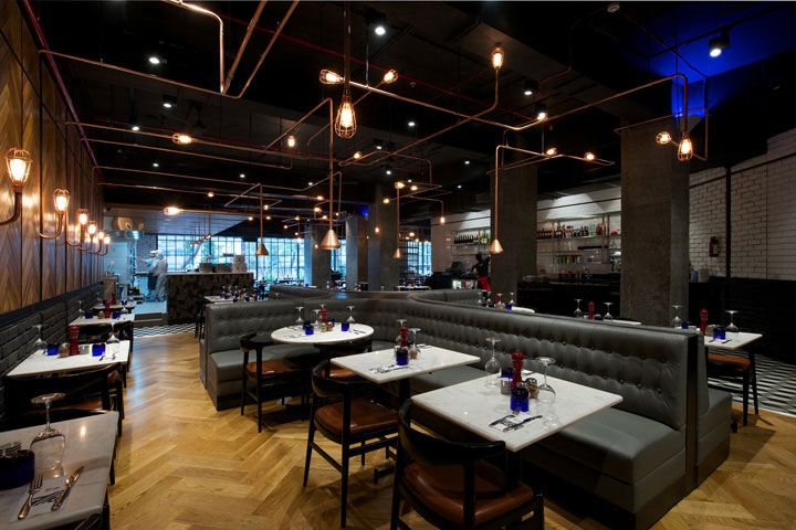 an empty restaurant with wooden floors and gray couches, white tablecloths and lights hanging from the ceiling