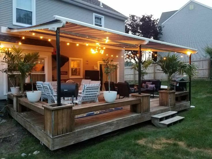 a deck with chairs and lights on it in front of a house that has an attached patio