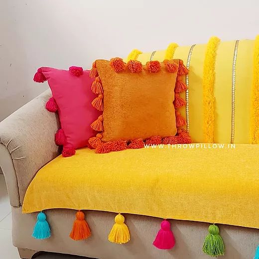 a yellow couch with colorful pillows and tassels on the pillowcase is sitting in front of a white wall