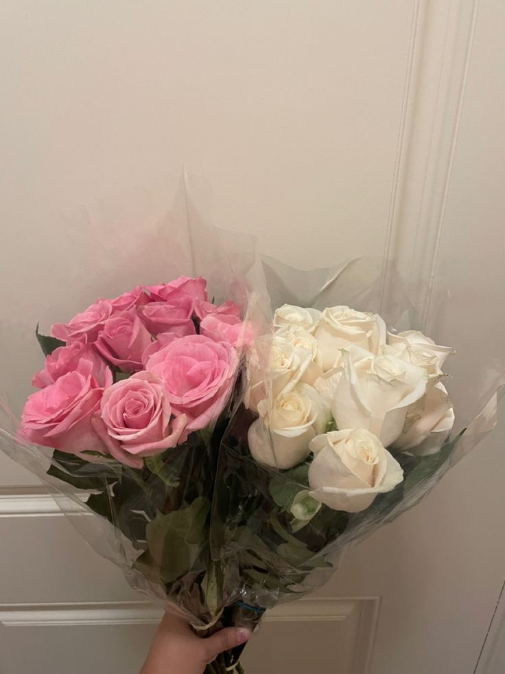 a person holding two large bouquets of white and pink roses in front of a door